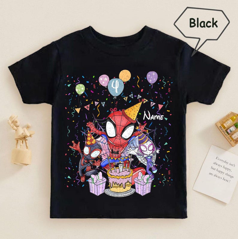 May include: Black t-shirt featuring a colorful graphic of Spider-Man characters celebrating a birthday. The design includes a cake, balloons, and the number 4. The word "Name" is also visible. The shirt is a short-sleeved style.