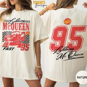 Puede incluir: Camiseta crema de Lightning McQueen. La parte delantera presenta un gr&aacute;fico rojo del personaje, el texto "Lightning McQueen", "THINK FAST" y el n&uacute;mero "95". La parte trasera muestra un gran "95" y "Lightning McQueen" en rojo y negro.