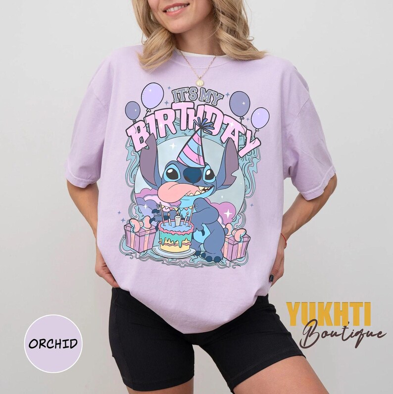May include: A lilac t-shirt with a cartoon character design, a birthday cake, and the text "IT'S MY BIRTHDAY". The graphic includes balloons and presents. The shirt is a relaxed fit.