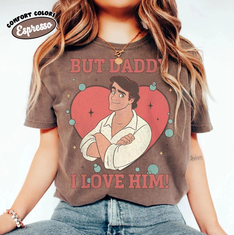 以下が含まれることがあります： エスプレッソ色のTシャツ。赤いハートの中に男性の漫画イラストがあり、その上下に「BUT DADDY I LOVE HIM！」の文字。ヴィンテージ感のあるデザインで、左上にComfort Colorsのロゴが入っています。