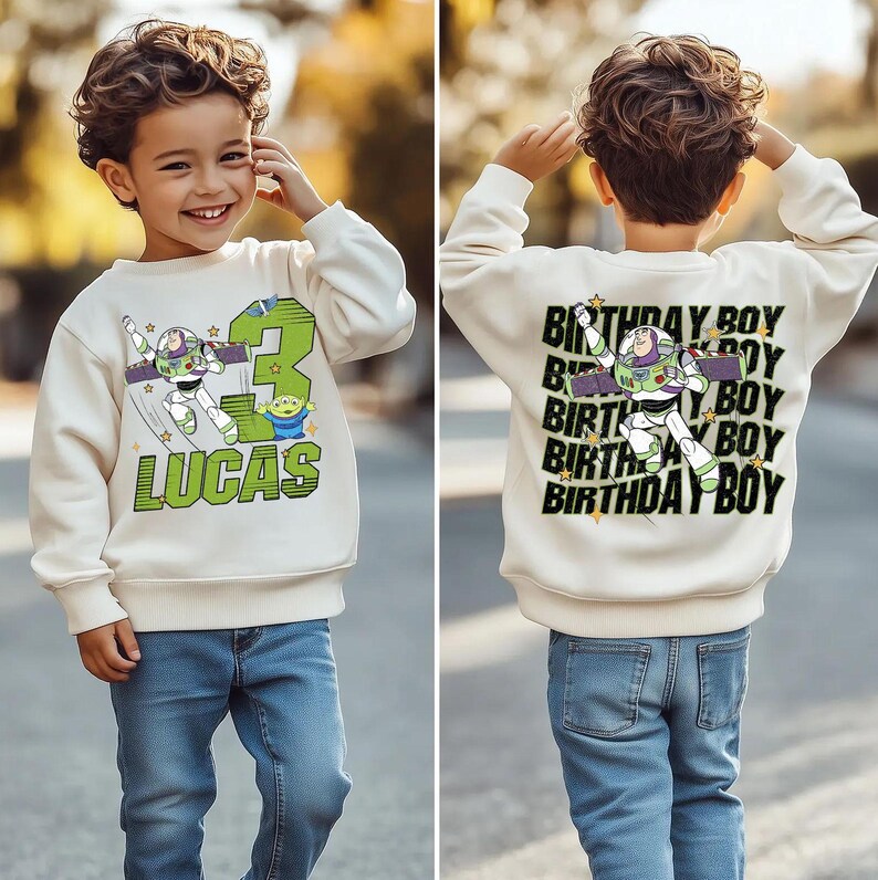 May include: A cream-colored sweatshirt featuring a Buzz Lightyear graphic, the number 3, and the name "LUCAS" in green. The back of the sweatshirt says "BIRTHDAY BOY" with a Buzz Lightyear graphic. The child is wearing blue jeans.