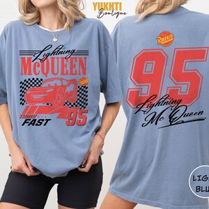 Puede incluir: Camiseta azul claro con dise&ntilde;o de Lightning McQueen. El frente presenta un coche rojo, el texto "Lightning McQueen" y el n&uacute;mero "95". La parte trasera muestra un gran "95" y "Lightning Mc Queen" en rojo y negro.