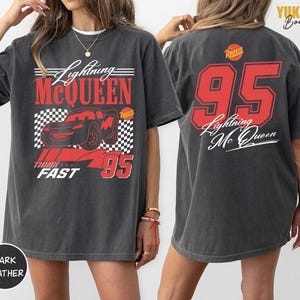 Puede incluir: Camiseta gris oscuro con dise&ntilde;o de Lightning McQueen. La parte delantera muestra el coche, el texto "Lightning McQueen", "Think Fast" y el n&uacute;mero 95 en rojo. La parte trasera tiene un gran 95 rojo y el texto "Lightning Mc Queen".