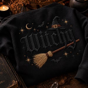 Peut inclure: Un sweat-shirt noir avec une broderie sombre du mot Witchy dans une police gothique. Le motif comprend un balai marron, un chapeau de sorcière avec une boucle dorée, un croissant de lune, deux petites chauves-souris et des étoiles dorées.