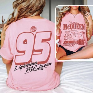 Puede incluir: Camiseta rosa claro con el n&uacute;mero "95" y las palabras "Lightning McQueen" en color granate. La camiseta tambi&eacute;n tiene el logotipo "Rusteze". La parte delantera de la camiseta tiene un gr&aacute;fico de Rayo McQueen con el texto "Lightning McQueen" y "Think Fast".