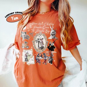 May include: Orange t-shirt with a graphic design featuring characters and text from "The Nightmare Before Christmas." The design includes Jack and Sally in an oval frame, along with other characters. The shirt has the text "Comfort Colors" and "Yam."