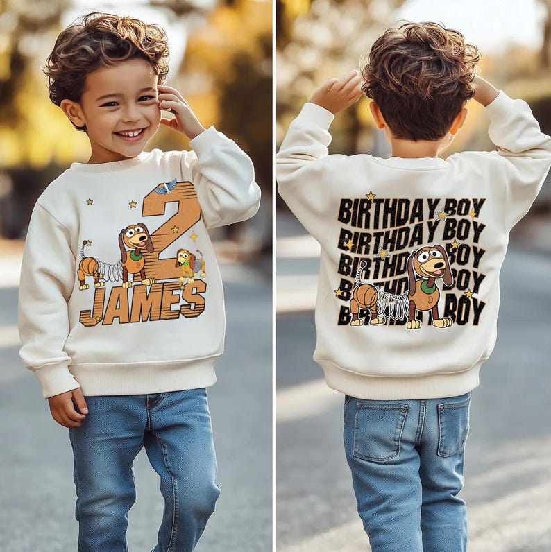 May include: Cream-colored sweatshirt with a cartoon dog and the number 2, with the name "JAMES" in a brown font. The back of the sweatshirt says "BIRTHDAY BOY" multiple times with a cartoon dog. The child is wearing blue jeans.