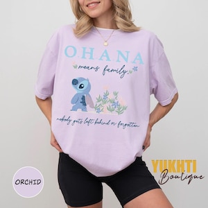 May include: A light purple t-shirt with the text "OHANA means family" and a cartoon character illustration. The shirt also has the phrase "nobody gets left behind or forgotten". The shirt is part of the Orchid collection.