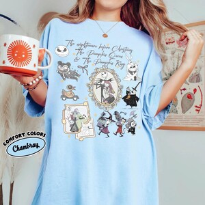 May include: Light blue t-shirt featuring characters and text from "The Nightmare Before Christmas." The design includes Jack Skellington, Sally, and other characters in a framed design. The shirt also has the text "The Nightmare Before Christmas & The Pumpkin King."