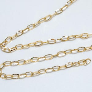 Op de afbeelding: Een spoel goudkleurige ketting met ovale schakels. Een lengte van de ketting is afgewikkeld en ligt op een wit oppervlak. De ketting wordt waarschijnlijk gebruikt voor het maken van sieraden of andere knutselprojecten. De ketting heeft een heldere, glanzende goudkleur.