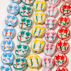 Peut inclure: Collection de perles en céramique peintes à la main. Chaque perle présente un motif floral différent en bleu, vert, jaune, rose et rouge. Les perles rondes ont un petit trou pour l'enfilage, parfait pour la création de bijoux.