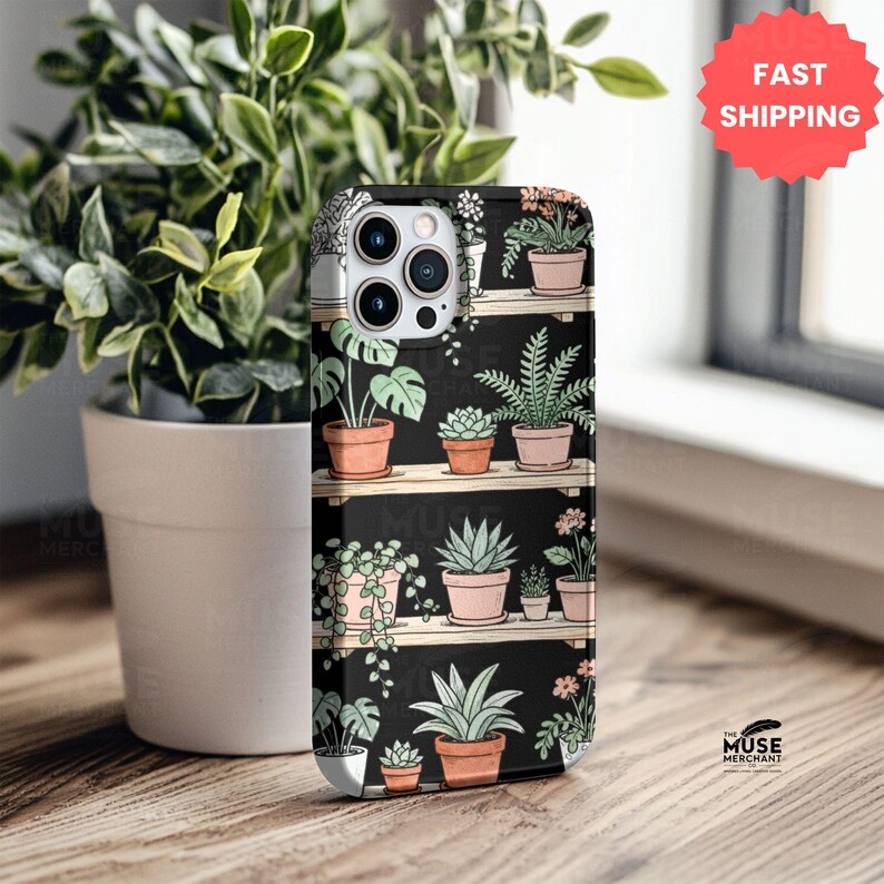 Puede incluir: Funda de tel&eacute;fono negra con un dise&ntilde;o bot&aacute;nico de plantas en macetas sobre estantes de madera. La funda tiene un acabado mate y un recorte para la c&aacute;mara. El logotipo de The Muse Merchant es visible en la parte inferior derecha.