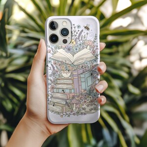 Puede incluir: Funda de teléfono blanca con una ilustración fantástica de un libro abierto, flores, setas y una taza de té. Una pequeña abeja vuela cerca de la parte superior. La funda tiene un acabado brillante.