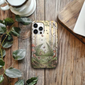 Op de afbeelding: Telefoonhoesje met een bosillustratie, inclusief berken, paddenstoelen en een vos. Het ontwerp toont vlinders, varens en een konijn in gedempte tinten. Gepresenteerd op een houten oppervlak.