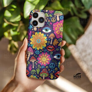May include: A phone case with a vibrant, psychedelic design. The case has a dark blue base, adorned with colourful flowers, mushrooms, eyes, lips, and peace symbols. The case is held in a hand, highlighting the intricate details and bright colours.