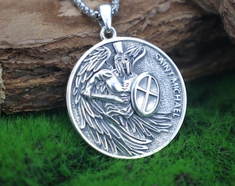 May include: A silver pendant necklace. The pendant is round and features a detailed depiction of Saint Michael, with wings, a shield, and a sword. The words "Saint Michael" are around the edge. The chain is also silver.