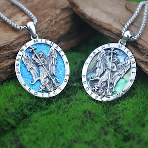 May include: Two silver Saint Michael pendants on chains. Each pendant features an oval design with the words "SAINT MICHAEL PROTECT US" around the edge. The center depicts Saint Michael with a cross and wings, set against a blue or iridescent background.