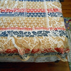 May include: A colorful bedspread with a patchwork design. The quilt features repeating patterns in red, blue, and gold, including floral and bird motifs. The bedspread is made of a textured fabric.