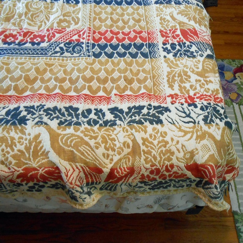 May include: A colorful bedspread with a patchwork design. The quilt features repeating patterns in red, blue, and gold, including floral and bird motifs. The bedspread is made of a textured fabric.
