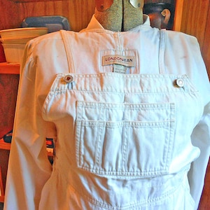 May include: White denim overalls with a bib pocket and adjustable straps. The overalls have a "LONDONJEAN" label and metal button closures. The garment is displayed on a mannequin.