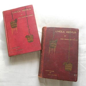 May include: Two vintage copies of "Uncle Remus" by Joel Chandler Harris. The books have red covers with gold lettering and illustrations of hanging baskets. The text "Illustrated by A.B. Frost" is also visible.