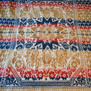 May include: A vintage, intricately patterned textile featuring a central starburst design in tan, red, and navy blue. The borders showcase floral and geometric motifs in complementary colors, creating a classic, ornate look.