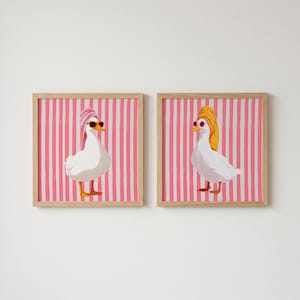 Peut inclure: Deux tableaux encadrés représentant des oies blanches portant des lunettes de soleil et des serviettes. L'une a une serviette rose, l'autre une serviette jaune. Le fond est à rayures roses et blanches.