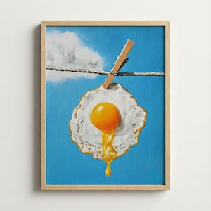 Könnte beinhalten: Gerahmtes Kunstwerk, das ein Spiegelei zeigt, das an einer Wäscheleine vor blauem Himmel mit einer Wolke hängt. Das Ei hat ein leuchtend gelbes Eigelb und weißes Eiweiß. Eine Holzklammer hält das Ei an Ort und Stelle.
