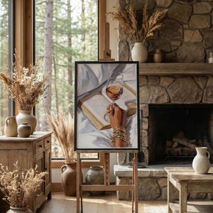 May include: A framed artwork on an easel depicts a glass of wine held over an open book. The painting features a hand adorned with gold bracelets. The room has a rustic aesthetic, with a stone fireplace, wooden furniture, and dried floral arrangements.