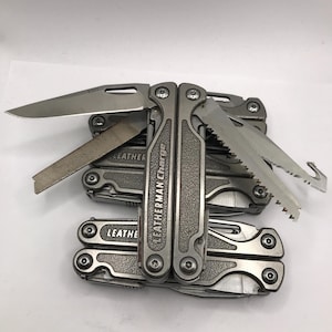 Peut inclure: Plusieurs outils multifonctions Leatherman Charge empilés, chacun avec une finition argentée. Les outils sont partiellement ouverts, révélant un couteau, une scie et une lime. Le logo Leatherman Charge est visible sur la poignée.