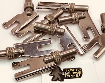 Könnte beinhalten: Eine Ansammlung silberfarbener Leatherman-Werkzeugteile, einige mit der Aufschrift "LEATHERMAN" und verschiedenen Nummern. Ein Aufkleber mit dem Text "I HAVE A LEATHERMAN I CAN HELP" ist ebenfalls zu sehen.