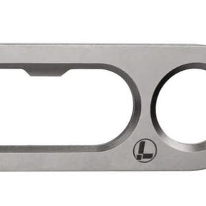 May include: A matte silver metal bottle opener with a rounded rectangular shape. It features a large elongated oval cutout on the left and a smaller circular cutout on the right. A small black logo consisting of a stylised letter L is printed on the surface.