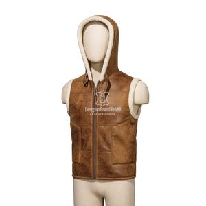 May include: A brown leather vest with a hood and a cream-colored shearling lining. The vest has a zip-up front and a logo on the chest. The vest is displayed on a mannequin.