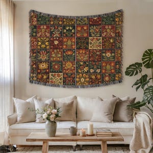 May include: A tapestry with a floral pattern in a grid design, featuring squares of flowers in shades of red, green, yellow, and cream. The tapestry is hung above a white sofa with neutral-colored pillows. The room has a cozy, inviting atmosphere.