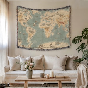 May include: A woven tapestry depicting a vintage world map in shades of blue, beige, and brown, with a fringed border. The map is hanging above a white sofa with beige pillows, creating a cozy living room setting.