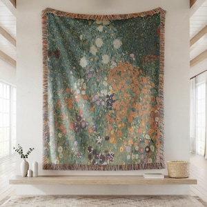 May include: A large, rectangular tapestry featuring a floral design in shades of green, orange, purple, and white. The tapestry is fringed along the edges and hangs on a white wall. The artwork depicts a field of flowers.