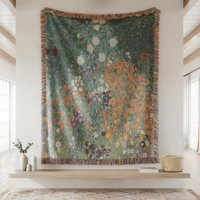 May include: A large, rectangular tapestry featuring a floral design in shades of green, orange, purple, and white. The tapestry is fringed along the edges and hangs on a white wall. The artwork depicts a field of flowers.