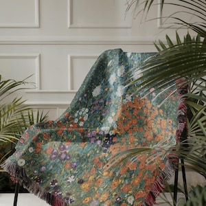 May include: A floral patterned throw blanket draped over a black metal chair. The blanket features a vibrant design of orange, white, purple, and yellow flowers on a green background. The edges are finished with a fringe.