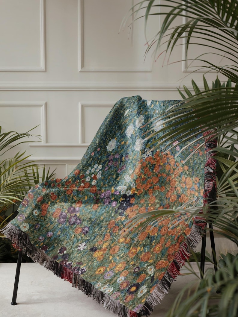May include: A floral patterned throw blanket draped over a black metal chair. The blanket features a vibrant design of orange, white, purple, and yellow flowers on a green background. The edges are finished with a fringe.