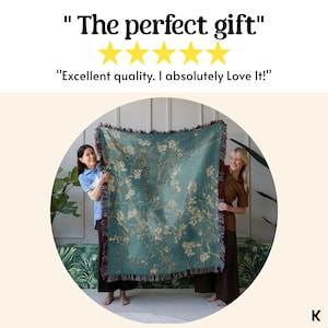 May include: A teal throw blanket featuring a floral design, held by two people. The blanket has a fringed edge and a pattern of white and beige flowers. Text above reads "The perfect gift" and "Excellent quality. I absolutely Love It!"