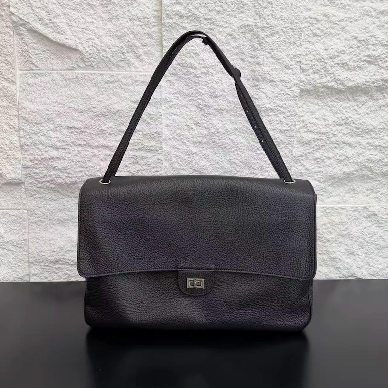 Front view of a black leather shoulder handbag featuring a wide flap cover, silver buckle lock, textured finish, and sleek design. A timeless everyday purse that blends modern elegance, practicality, and premium style for women’s fashion.