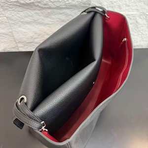 Detailed interior view of a black leather handbag featuring a contrasting red lining, large storage space, side compartments, and quality stitching. This elegant shoulder bag combines functionality with a luxurious design for women who appreciate practical fashion accessories.