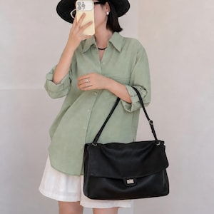 Fashionable woman carrying a black leather handbag with a structured shape, flap closure, and elegant silver lock detail. The bag adds a refined touch to any outfit while providing practical space and a comfortable shoulder carry style for daily fashion needs.