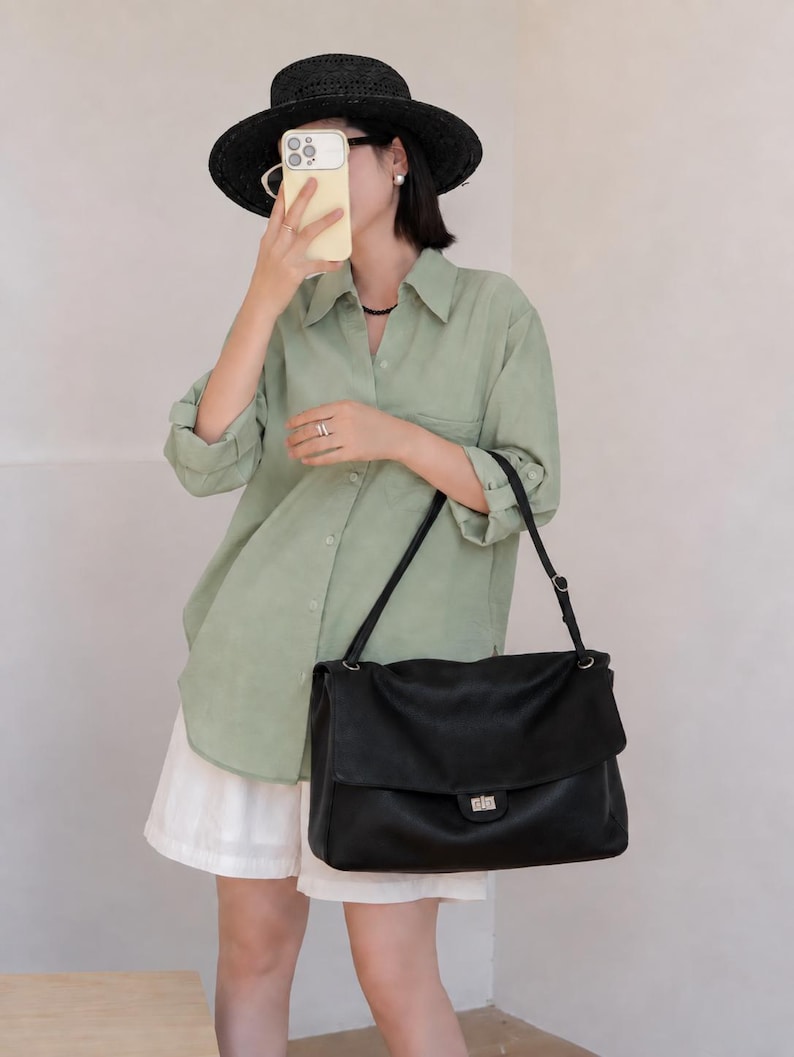 Fashionable woman carrying a black leather handbag with a structured shape, flap closure, and elegant silver lock detail. The bag adds a refined touch to any outfit while providing practical space and a comfortable shoulder carry style for daily fashion needs.