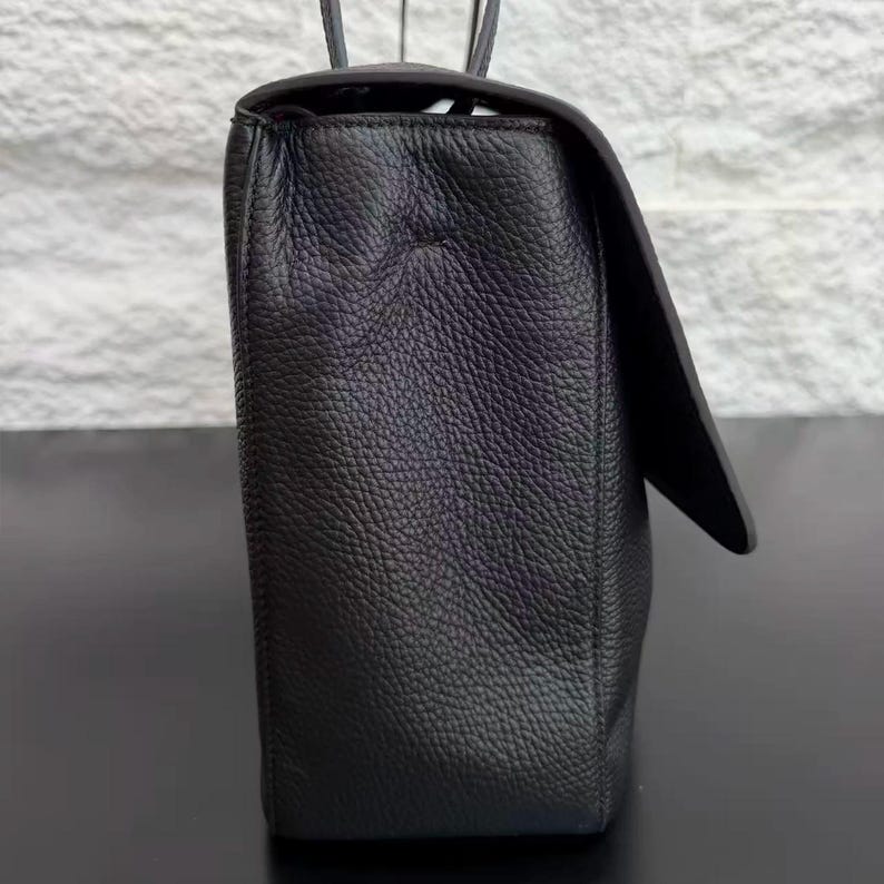 Side profile of a black leather handbag displaying its structured shape, sturdy construction, and textured leather surface. The elegant design includes a spacious body, refined stitching, and a comfortable shoulder strap, making it a versatile accessory for daily use.