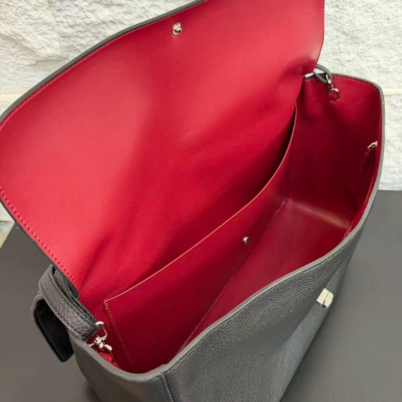 Open black leather handbag showing a spacious red interior lining with organized compartments and premium craftsmanship. The roomy inside provides practical storage for everyday essentials while the elegant exterior offers a sophisticated and stylish appearance.