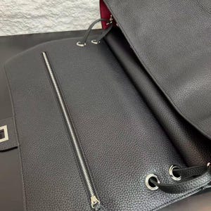Close-up view of a black pebbled leather handbag showcasing its spacious interior and handcrafted details. The bag features silver-tone metal eyelets, leather drawstring accents, a structured silhouette, and a contrasting burgundy lining. Captured in soft lighting, this image highlights the natural grain texture, premium craftsmanship, and elegant design of the minimalist leather shoulder bag.