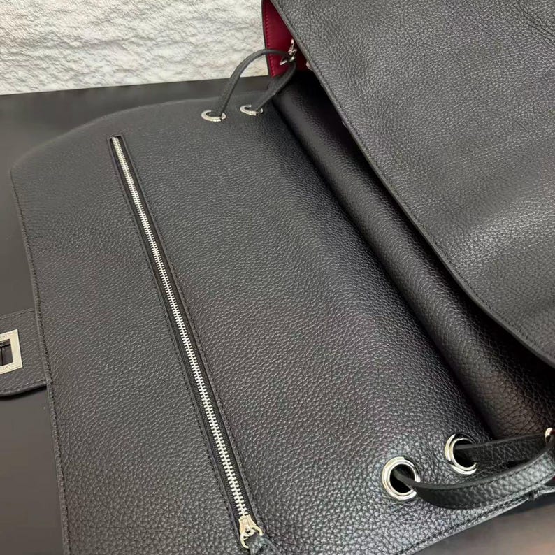 Close-up view of a black pebbled leather handbag showcasing its spacious interior and handcrafted details. The bag features silver-tone metal eyelets, leather drawstring accents, a structured silhouette, and a contrasting burgundy lining. Captured in soft lighting, this image highlights the natural grain texture, premium craftsmanship, and elegant design of the minimalist leather shoulder bag.