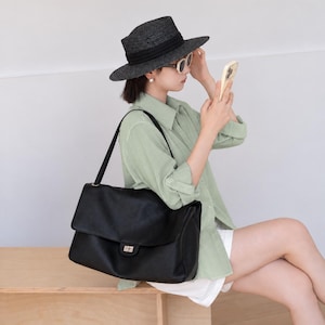 Black leather handbag shown in a lifestyle setting, highlighting its elegant silhouette, adjustable shoulder strap, flap cover, and secure metal lock closure. This versatile purse offers a sophisticated style with practical storage space for daily essentials.