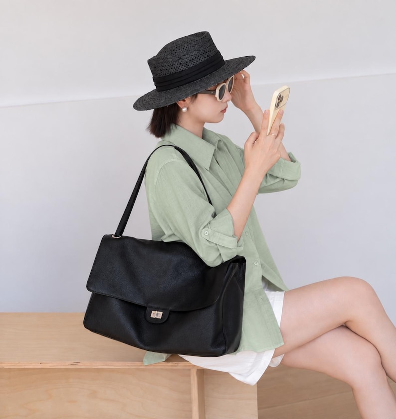 Black leather handbag shown in a lifestyle setting, highlighting its elegant silhouette, adjustable shoulder strap, flap cover, and secure metal lock closure. This versatile purse offers a sophisticated style with practical storage space for daily essentials.